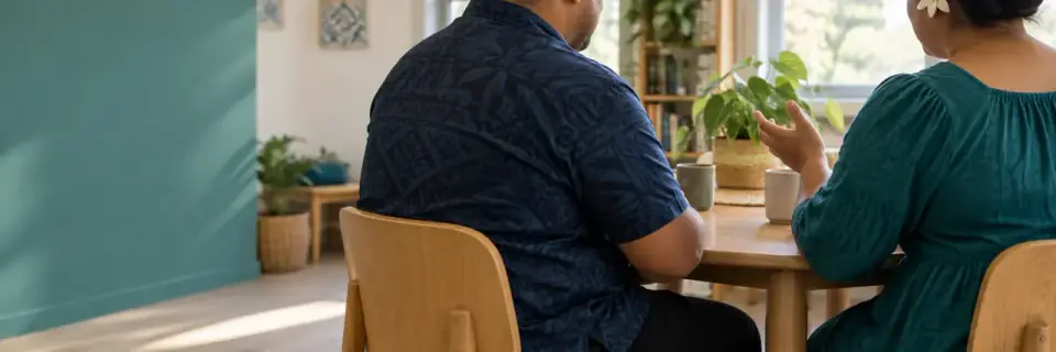 Two people talking together at a table over cups of tea.